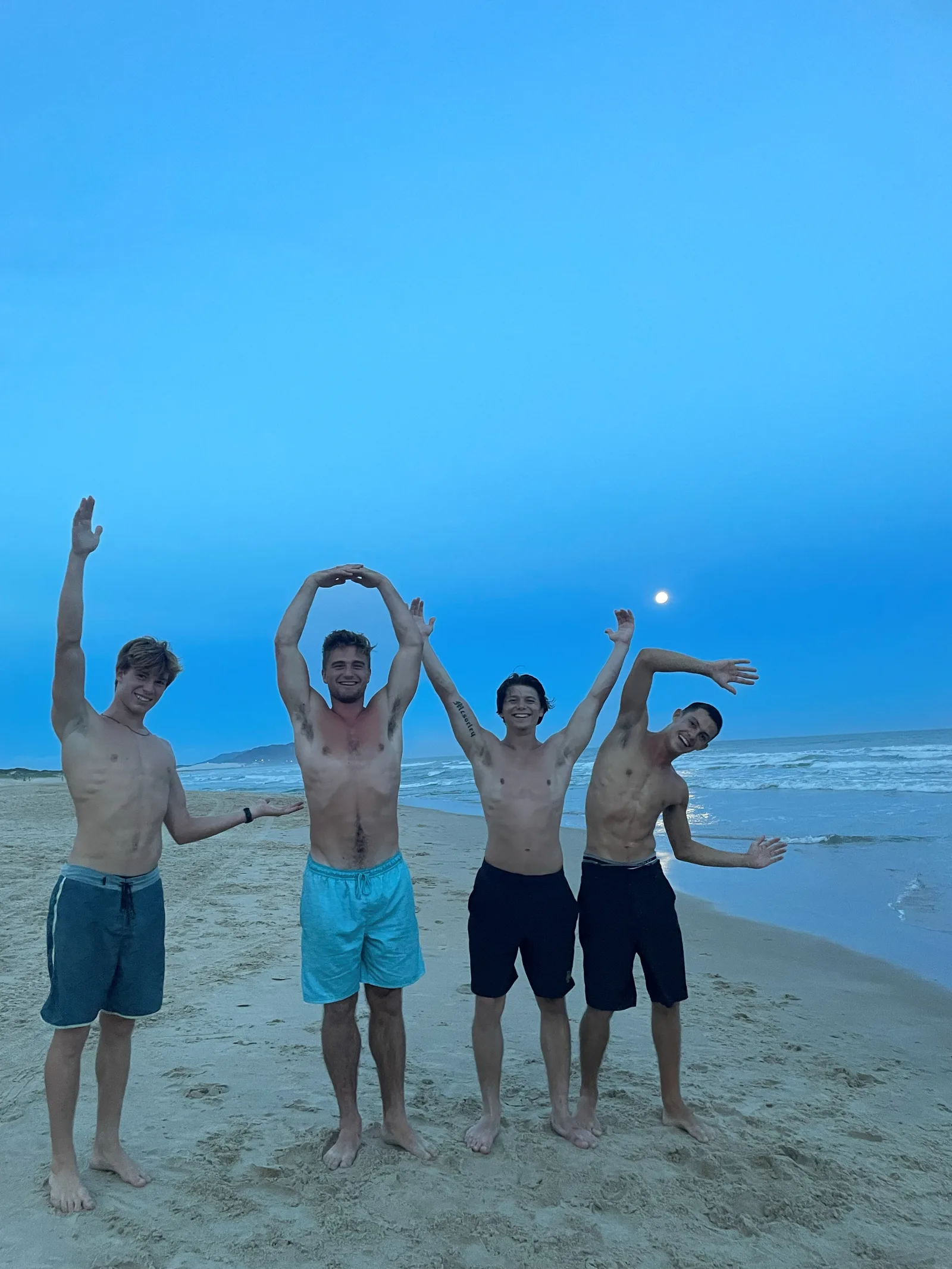Logan and three friends spelling out LOVE on the beach at dusk