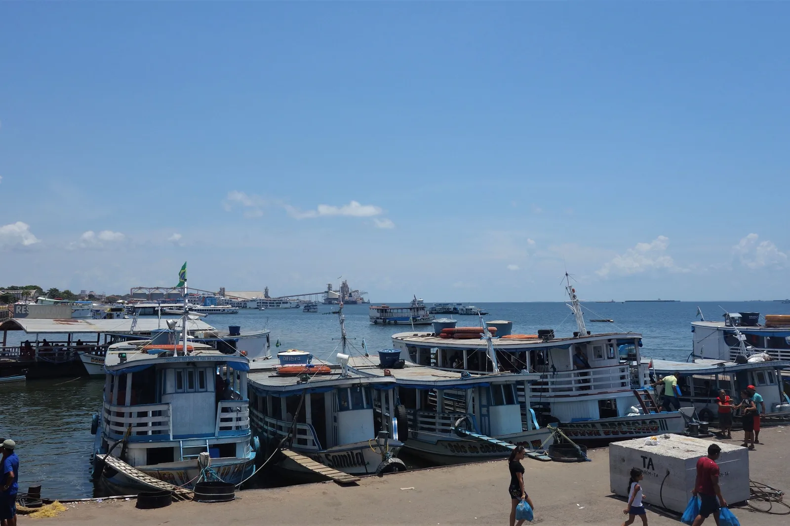Several white multi-deck passenger riverboats moored side by side at a busy quay, people and a small kiosk on the dock in front