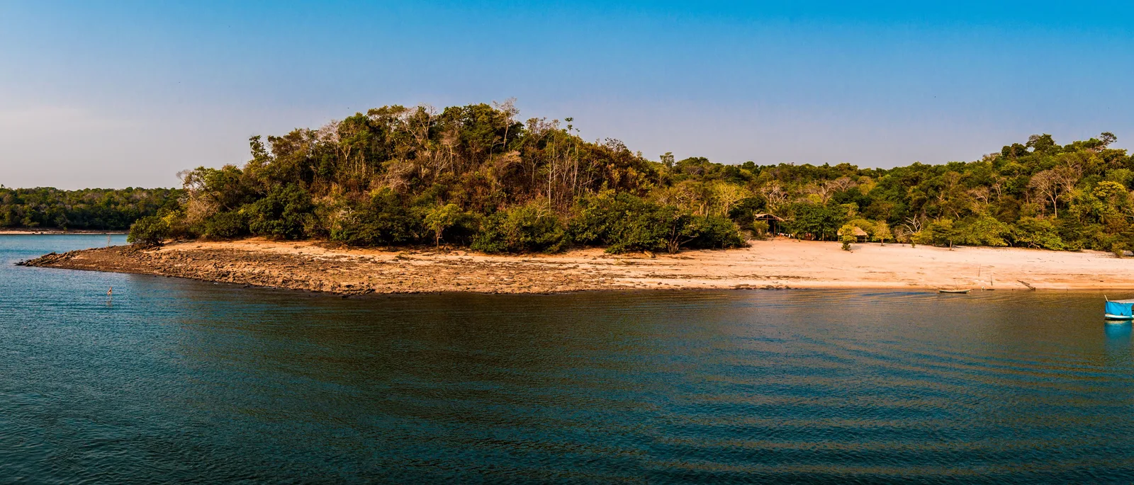 A wide panorama of a forested island fringed with white sand, set in calm blue water under a clear sky