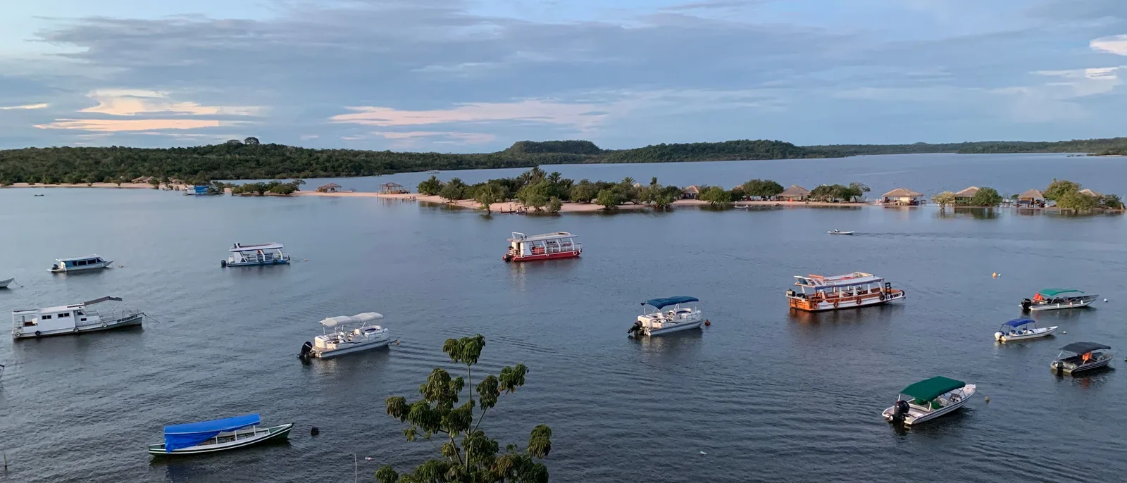 Small motorboats and canopied passenger boats moored in a wide bay seen from above, a low wooded island and a flat horizon behind