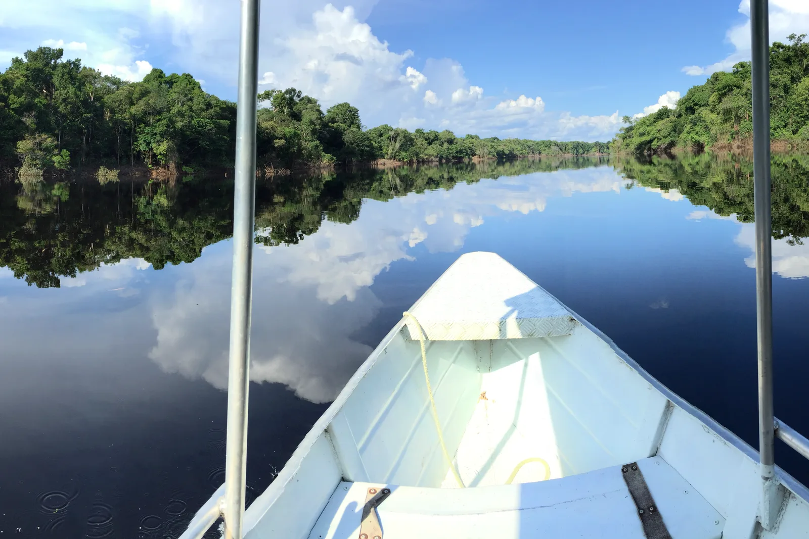 The white bow of a small boat pointing up a narrow channel of perfectly still water, forest and cloud reflected so cleanly that the horizon is hard to find