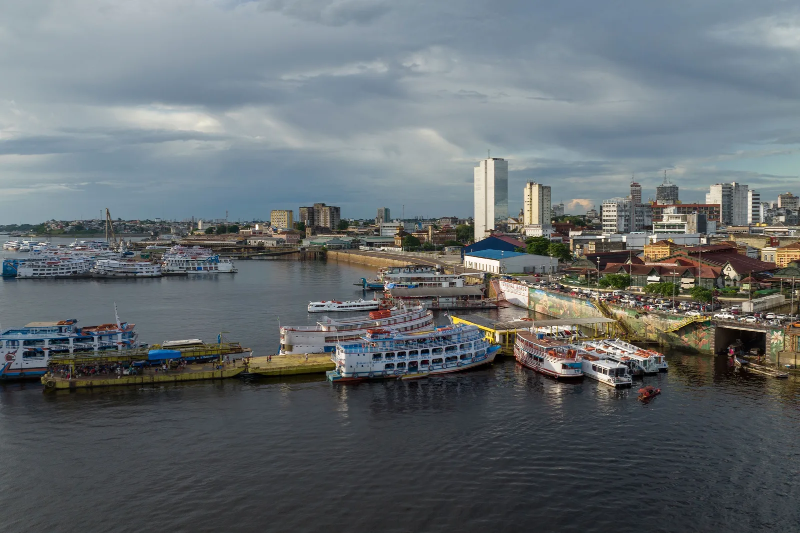 Manaus seen from the water: rows of double-decked riverboats moored along the shore with the dense low city and its tower blocks rising behind them