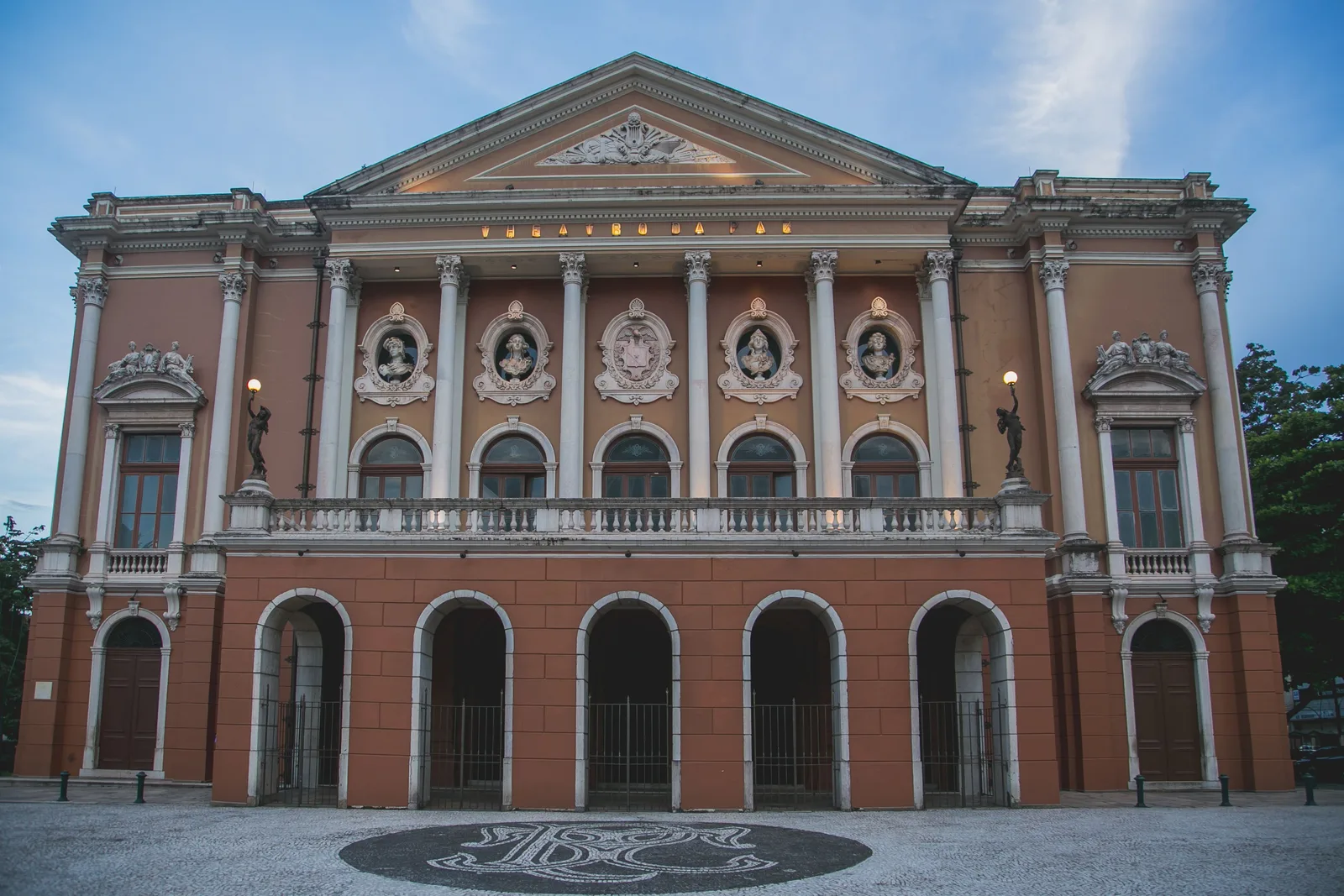 The front of the Theatro da Paz: a pink and cream neoclassical facade with a colonnade of tall columns under a sculpted pediment, seen straight on across its forecourt