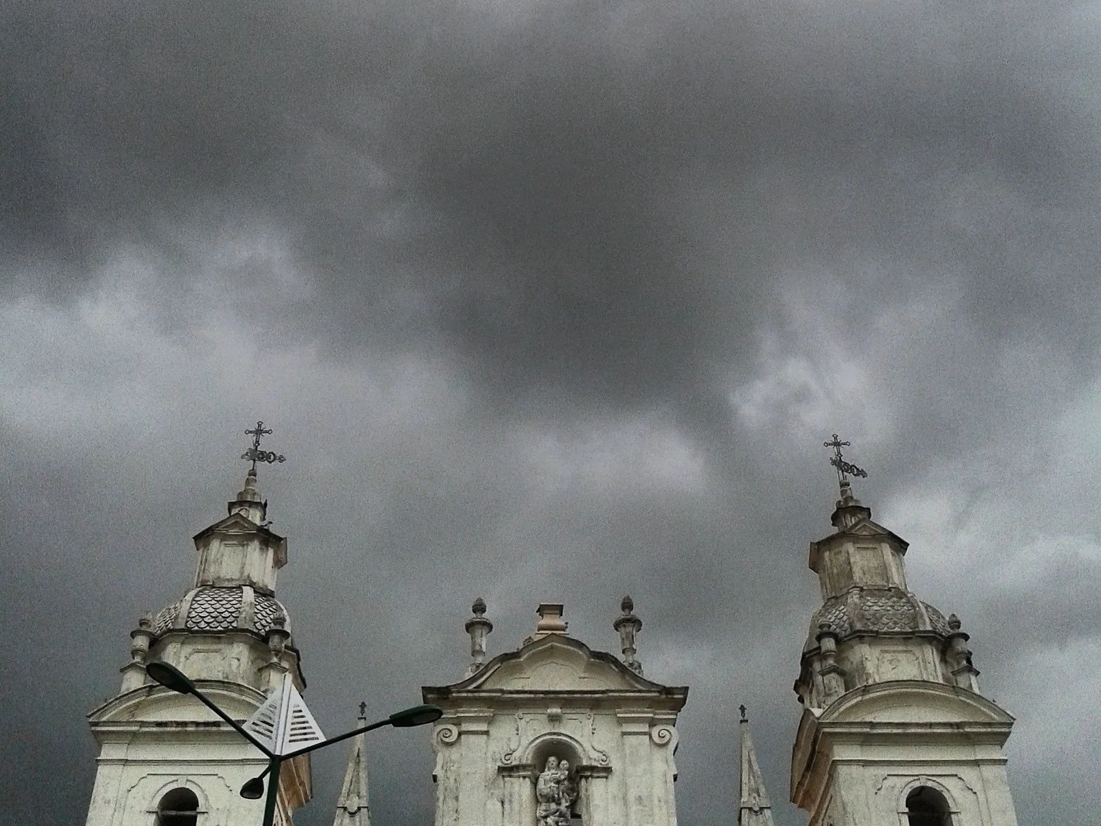 The pale twin towers and crosses of a church in Belém standing under a low, dark, heavily textured storm sky