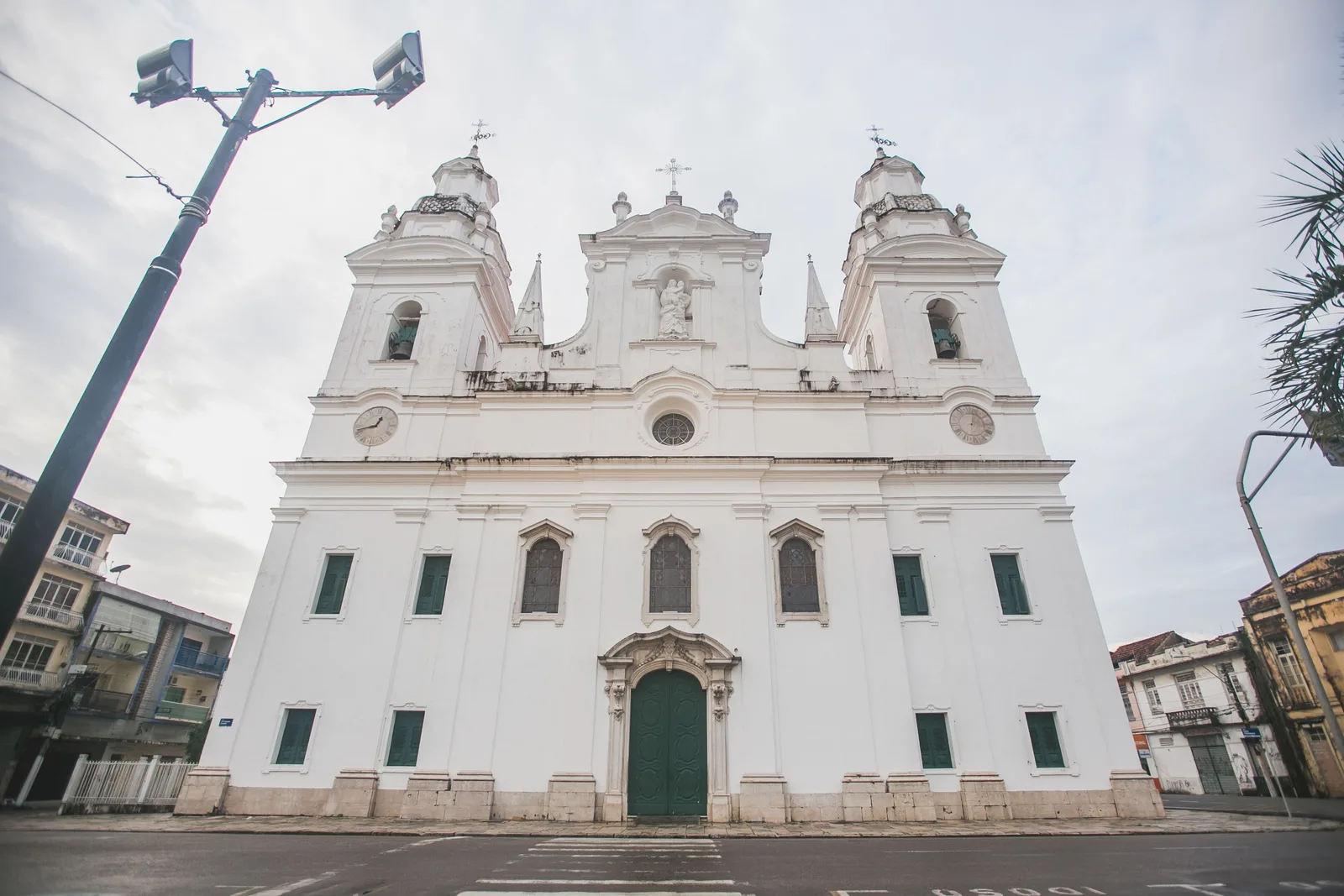 The white twin-towered front of the Catedral da Sé in Belém seen straight on under a flat pale sky, low buildings running away on either side