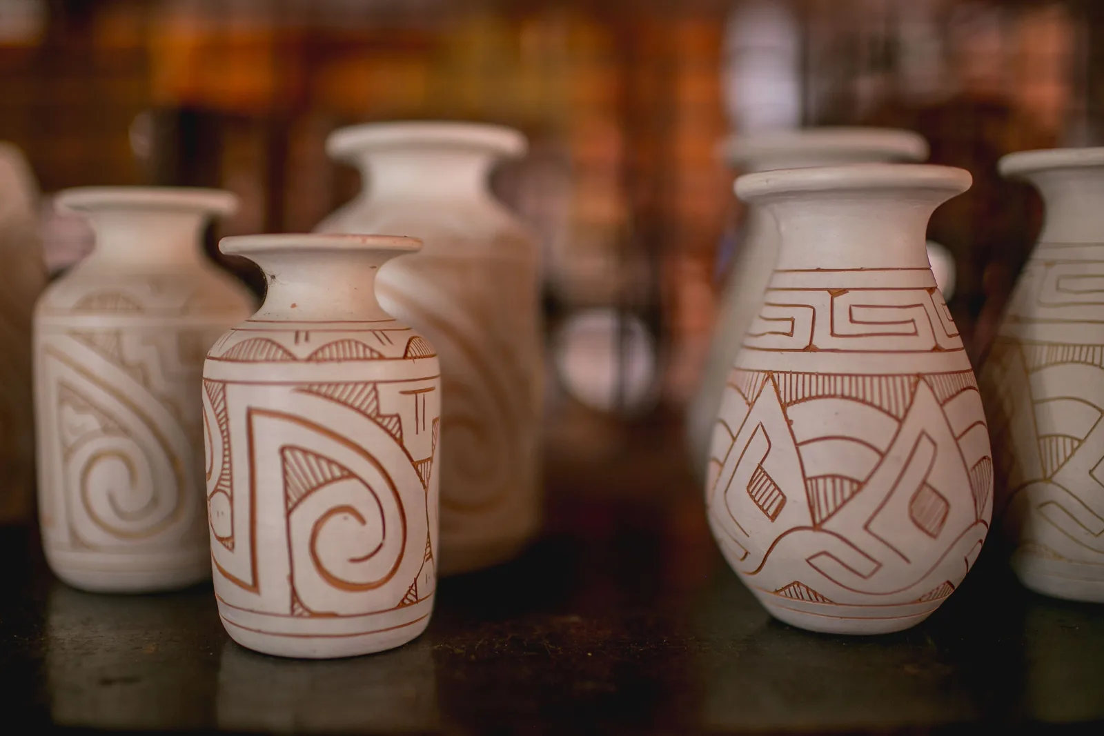 Pale unglazed pots lined up on a bench, each one cut with the swirling geometric line-work of Marajoara ceramics