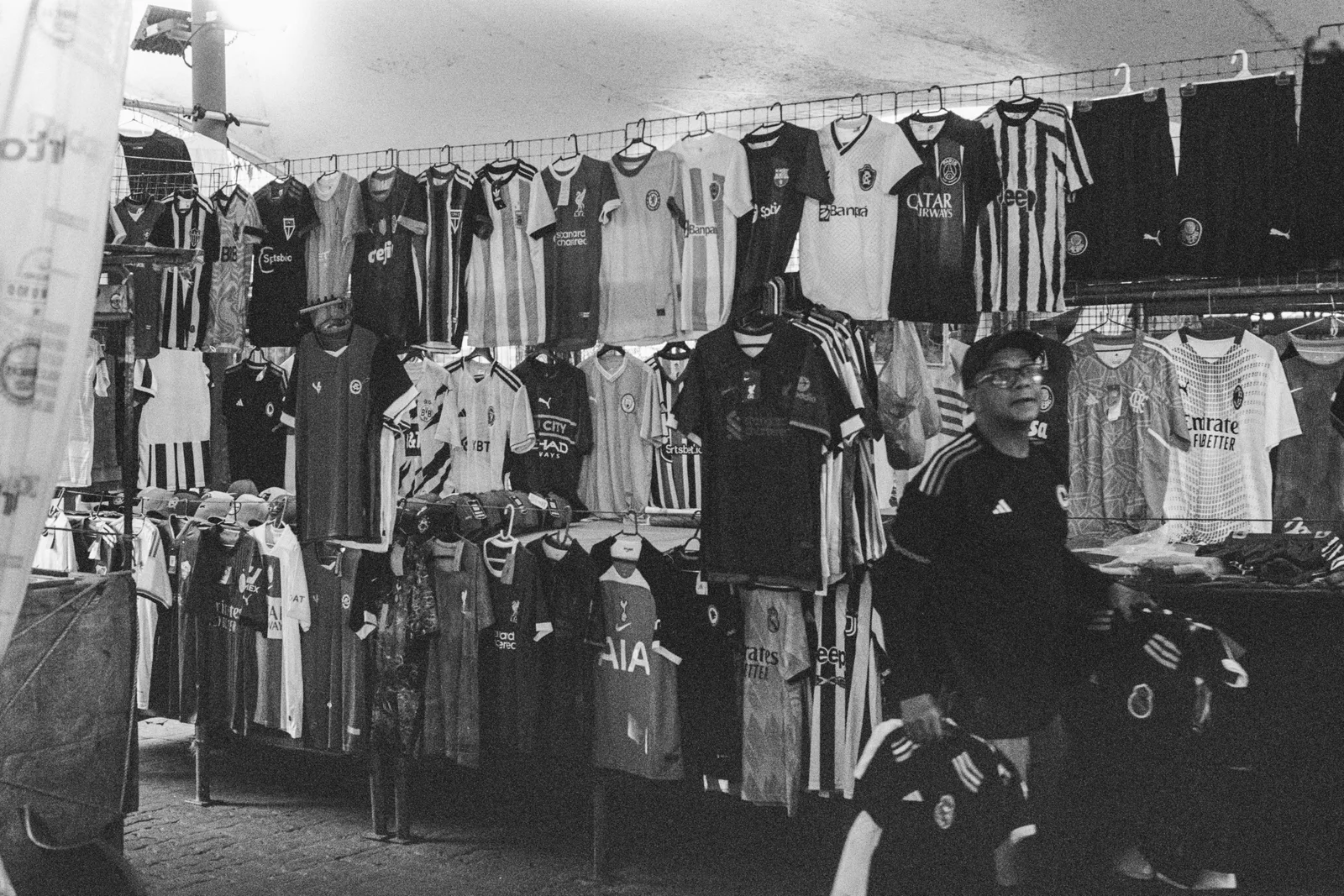 Black and white: rows of shirts and jerseys hung across a market stall at Ver-o-Peso, a trader standing among them