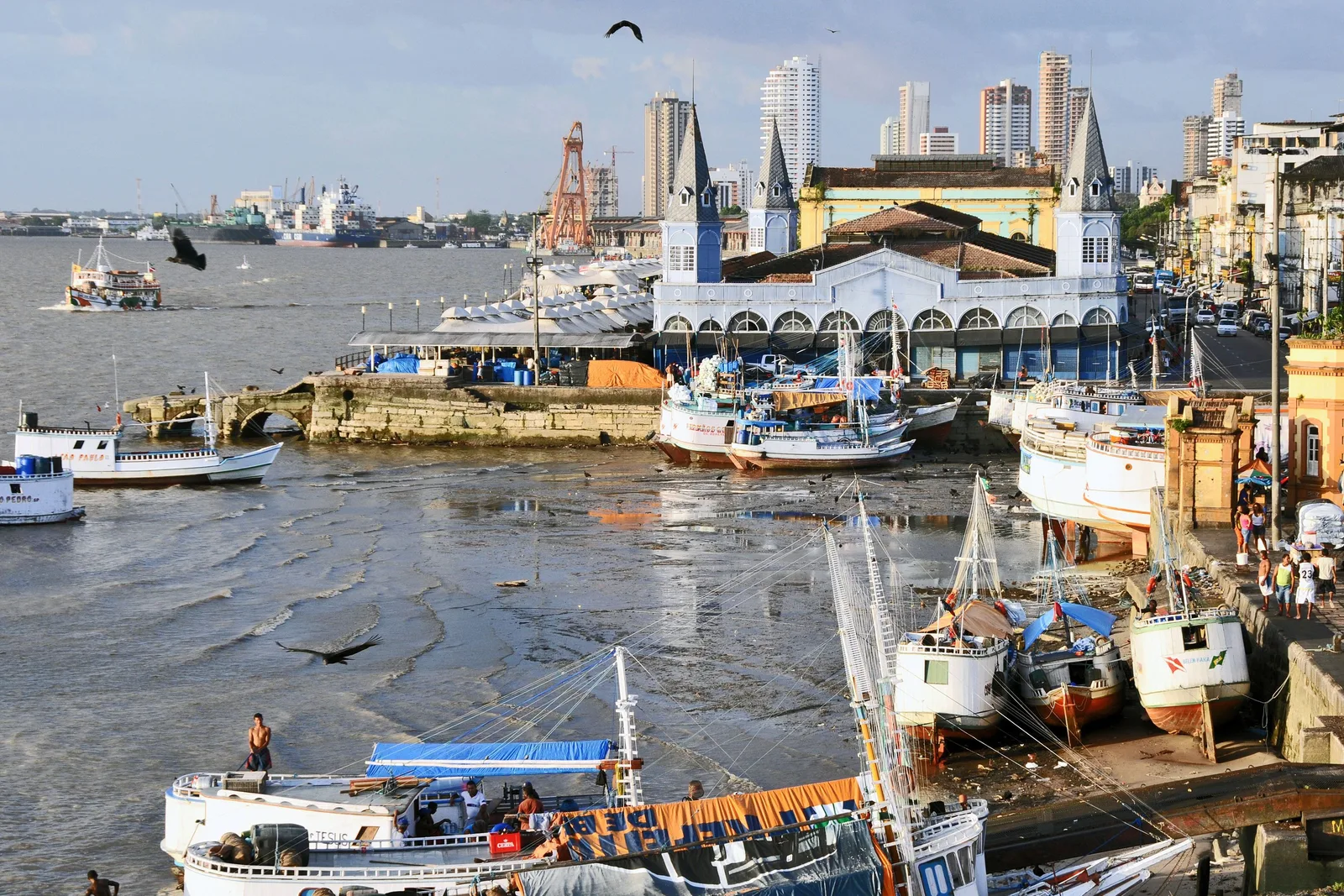 Wooden fishing boats crowded along the Ver-o-Peso waterfront with the iron market pavilion and its turrets behind them and city buildings beyond