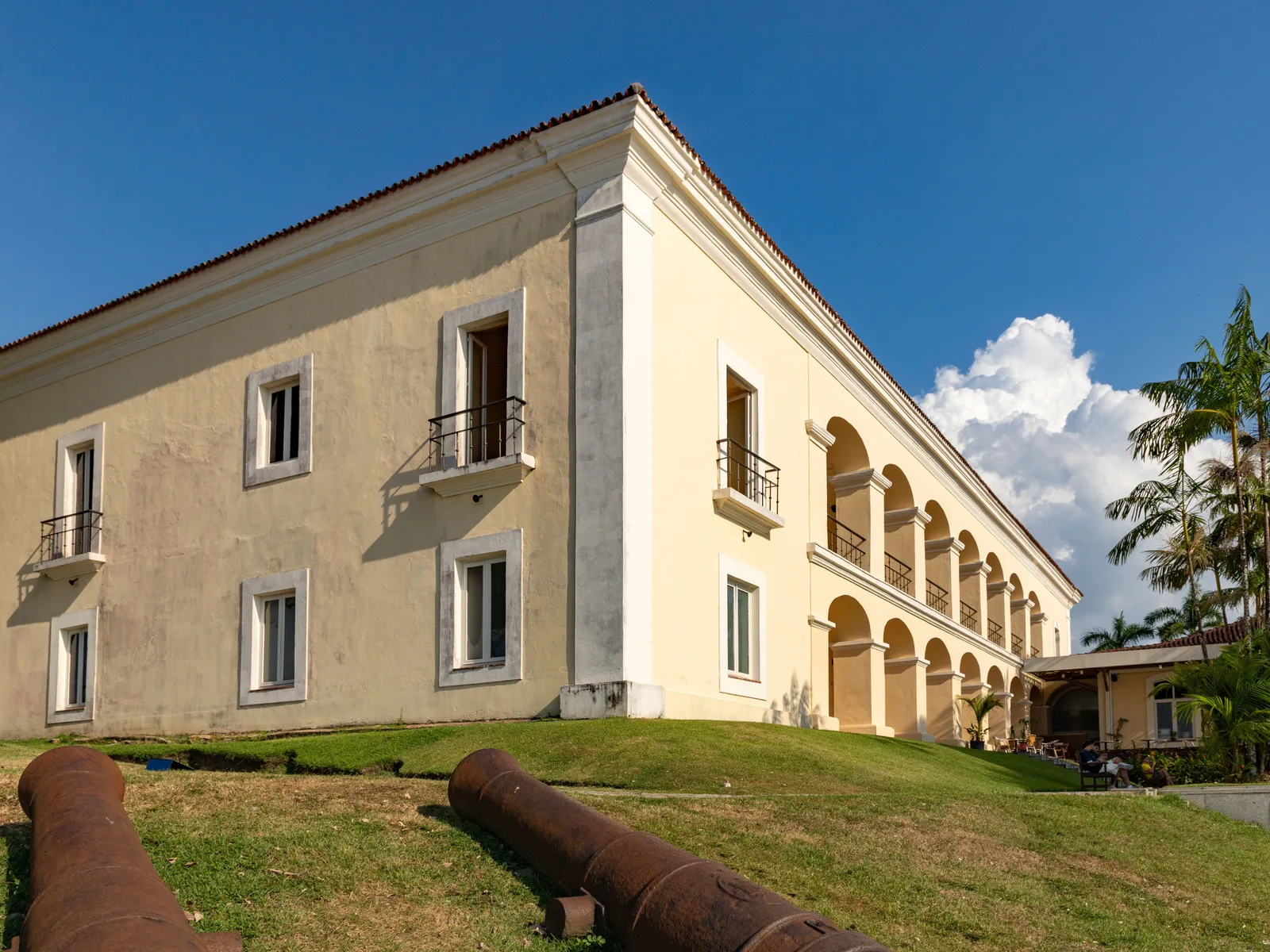 The Casa das Onze Janelas: a long two-story colonial house painted pale yellow with a first-floor arcade and iron balconies, two old cannons lying on the grass in front of it