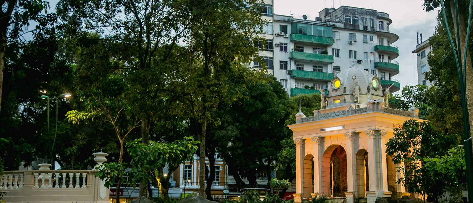 A leafy corner of the Praça da República in Belém: a yellow colonnaded pavilion under big shade trees, with apartment buildings rising close behind