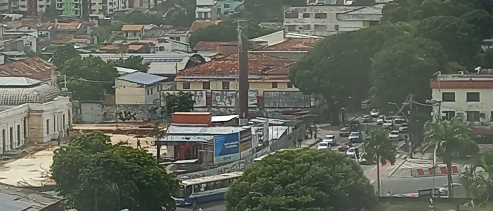 Central Belém seen from above: low tiled roofs and shopfronts packed along a busy street, traffic queuing between them and green trees breaking up the blocks
