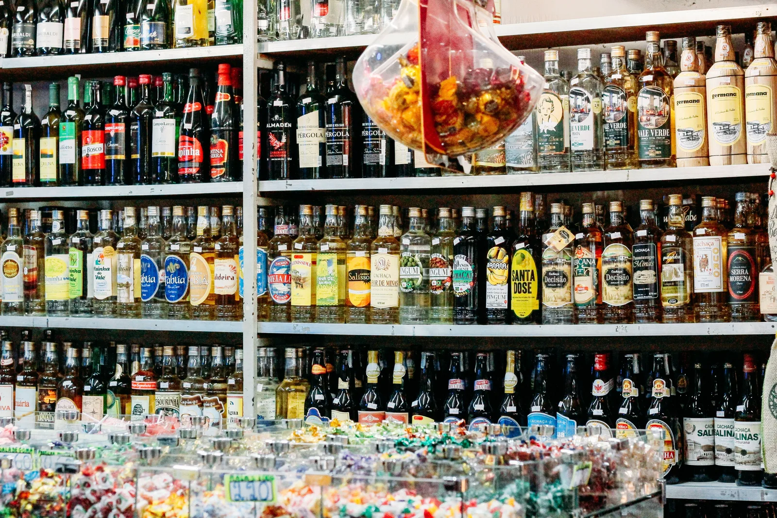 Floor-to-ceiling shelves of cachaça and liquor bottles in a Mercado Central shop, wrapped sweets heaped in open bins along the counter in front