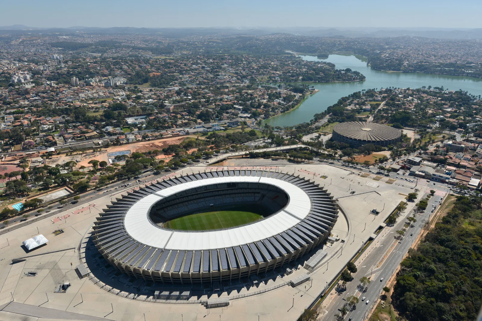 The Mineirão stadium from the air: a ring of concrete stands around a green pitch, the Pampulha lake and the low northern suburbs spreading behind it