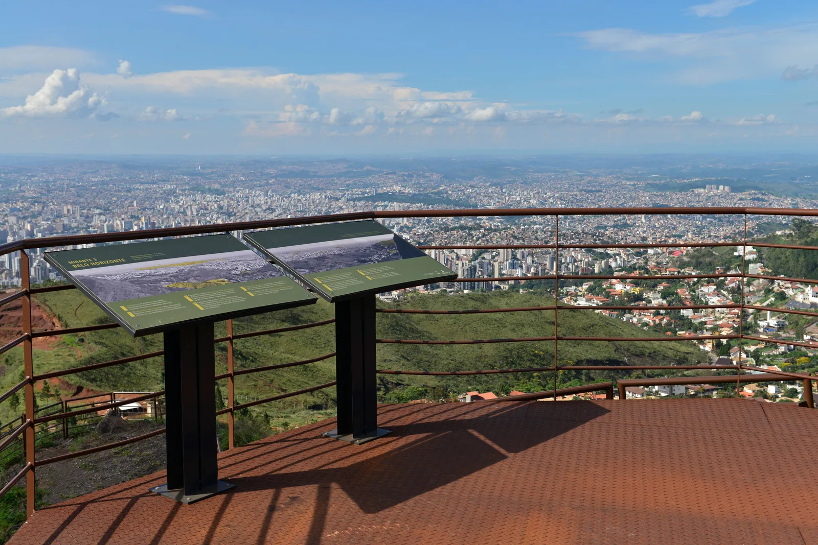 A rust-red viewing deck with information panels high on the Serra do Curral, the city spread out to the horizon far below under a blue sky