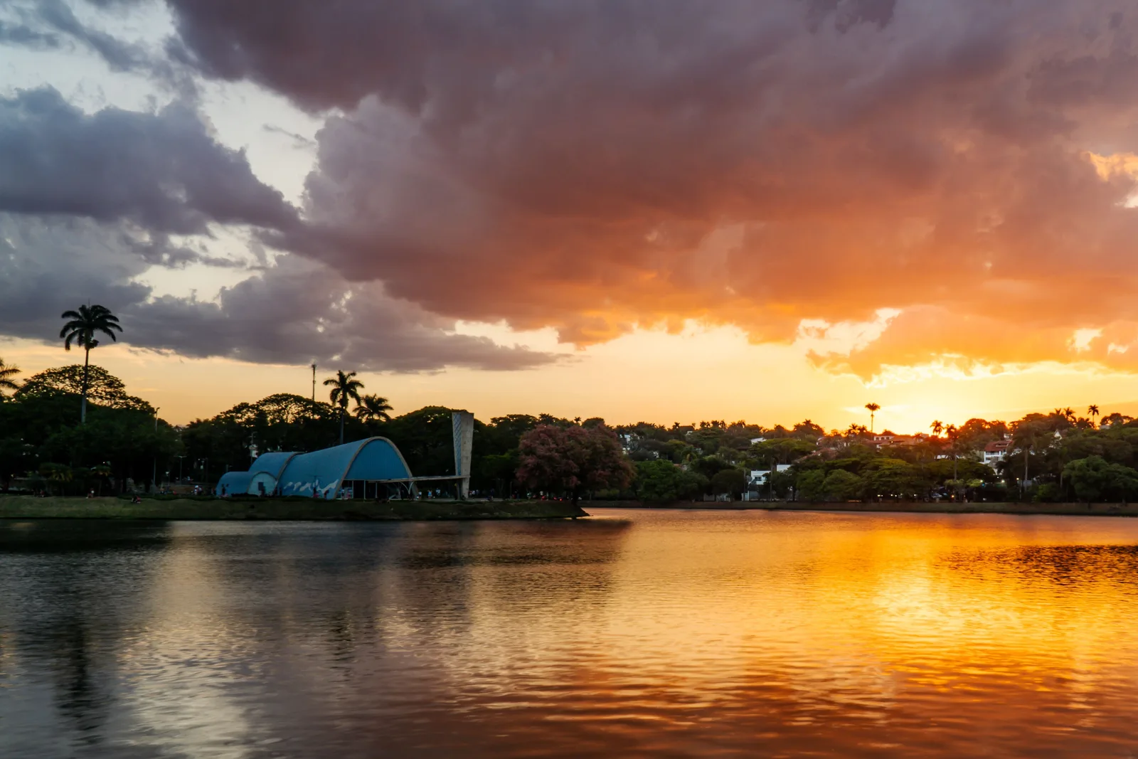 An orange sunset over the Pampulha lake, the low blue vault of the São Francisco de Assis church dark on the far shore and the sky reflected in the water
