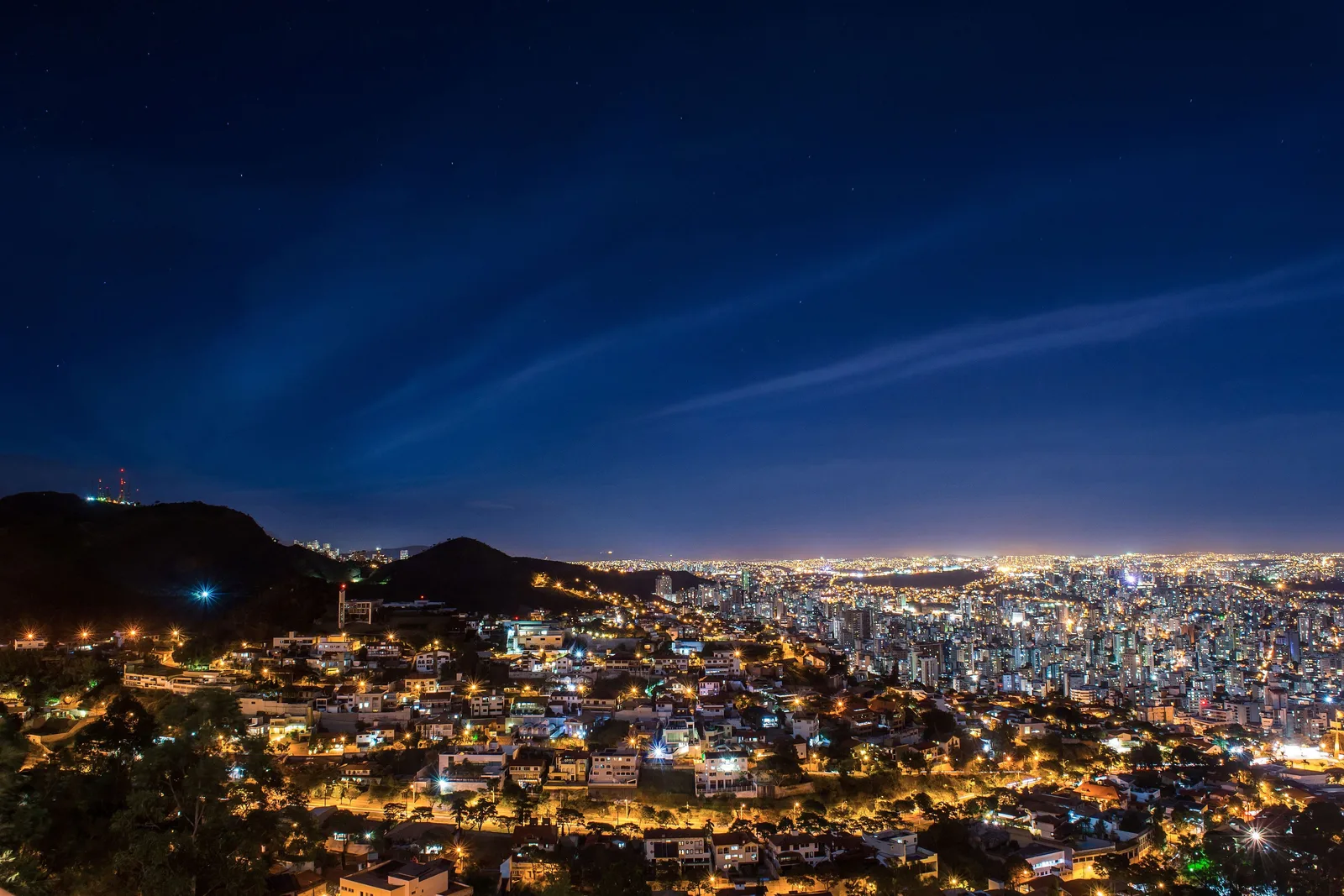 Belo Horizonte at night from a hillside, the lights of the city filling a wide valley under a deep blue sky