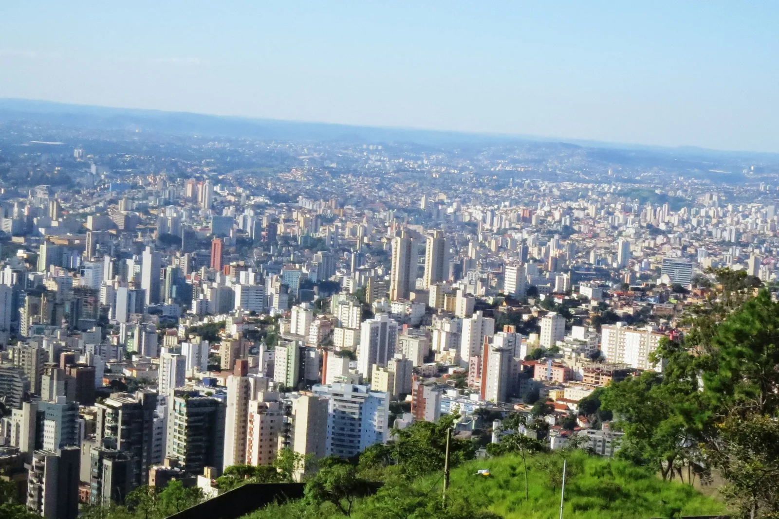 Belo Horizonte from the Mirante do Mangabeiras: a sea of white apartment towers spreading to the horizon under a pale blue sky, green slopes in the foreground
