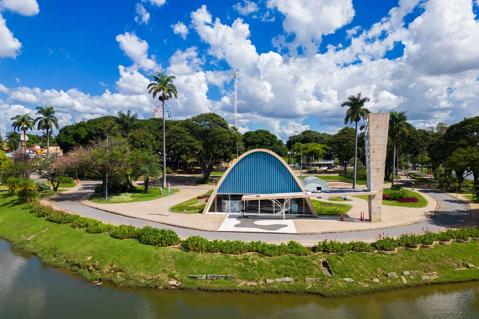 The Pampulha church from the air: its blue vaulted roof and bell tower on a lawn on the lake shore, the water and wooded shoreline curving around it