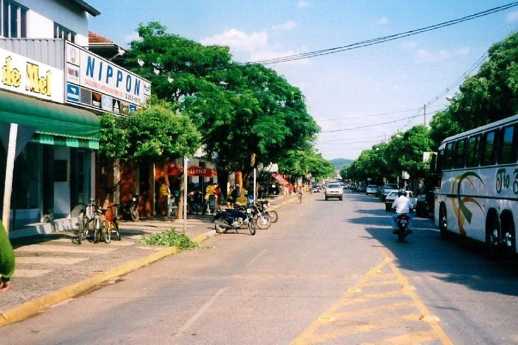 The wide, tree-lined main street of Bonito with shopfronts and awnings along one side, parked motorbikes and bicycles at the curb, a coach and a motorcyclist on the road