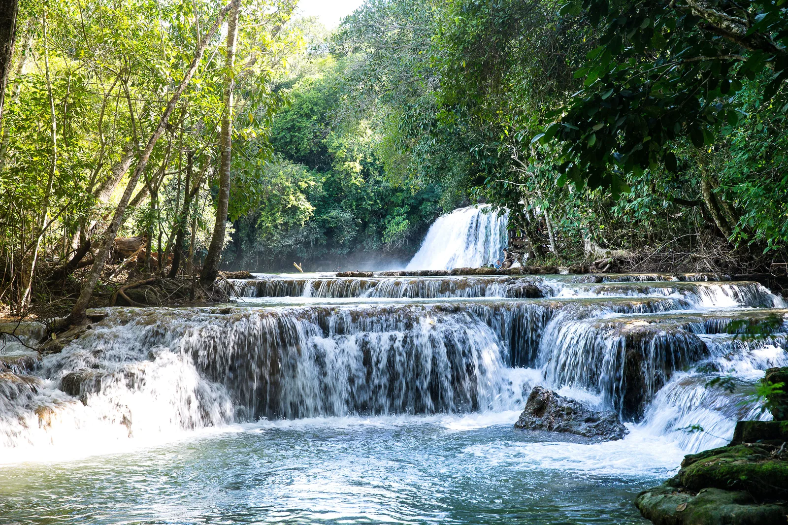 A staircase of wide travertine cascades on the Rio da Prata, white water spilling over three low moss-covered ledges into a turquoise pool
