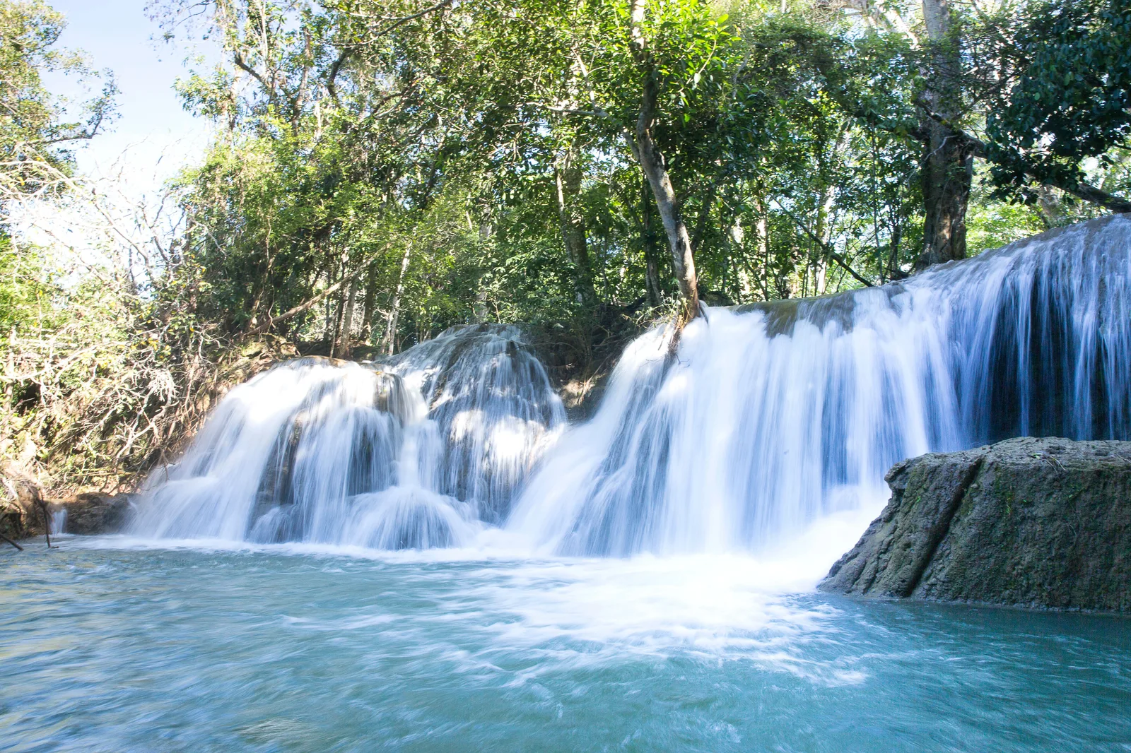 A wide travertine waterfall near Bonito dropping in a curtain over a green ledge into a turquoise pool