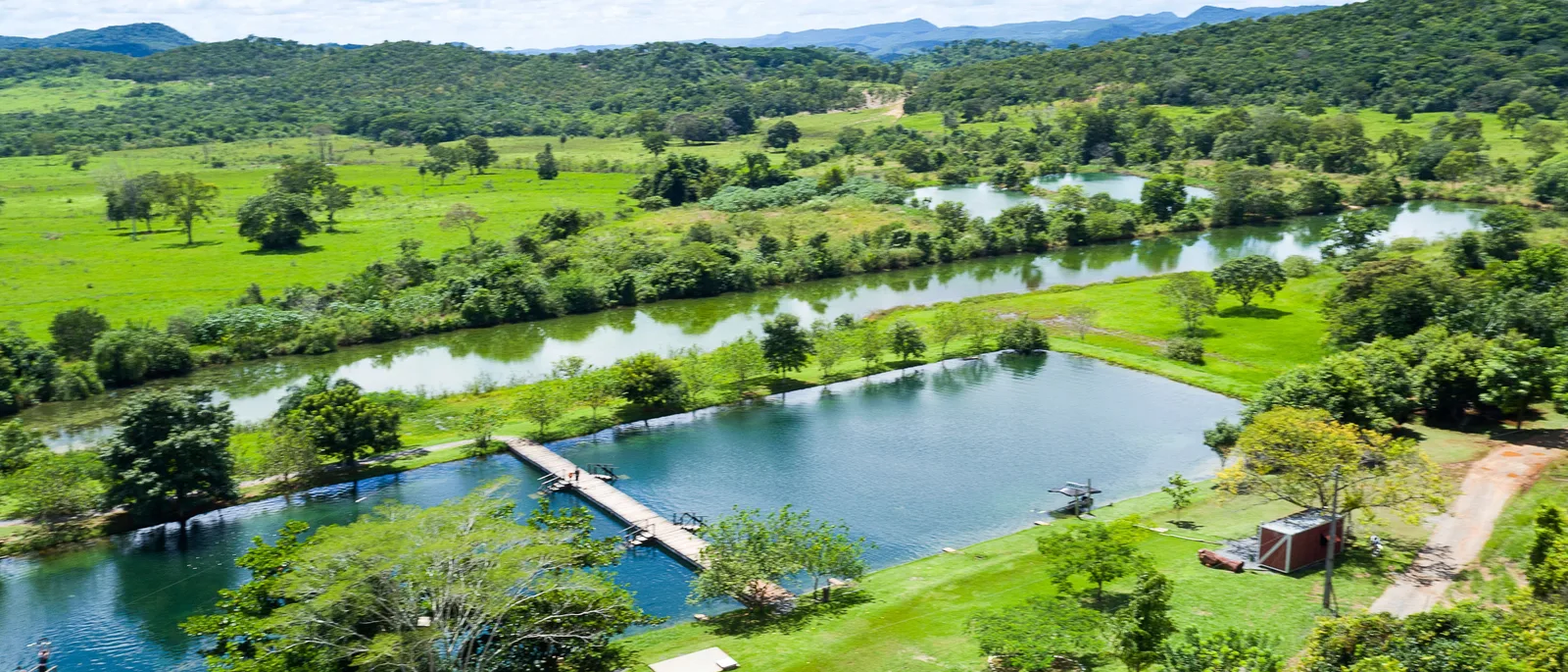 Green pasture and gallery forest from the air near Bonito, with a small lake, a jetty and farm buildings among the trees