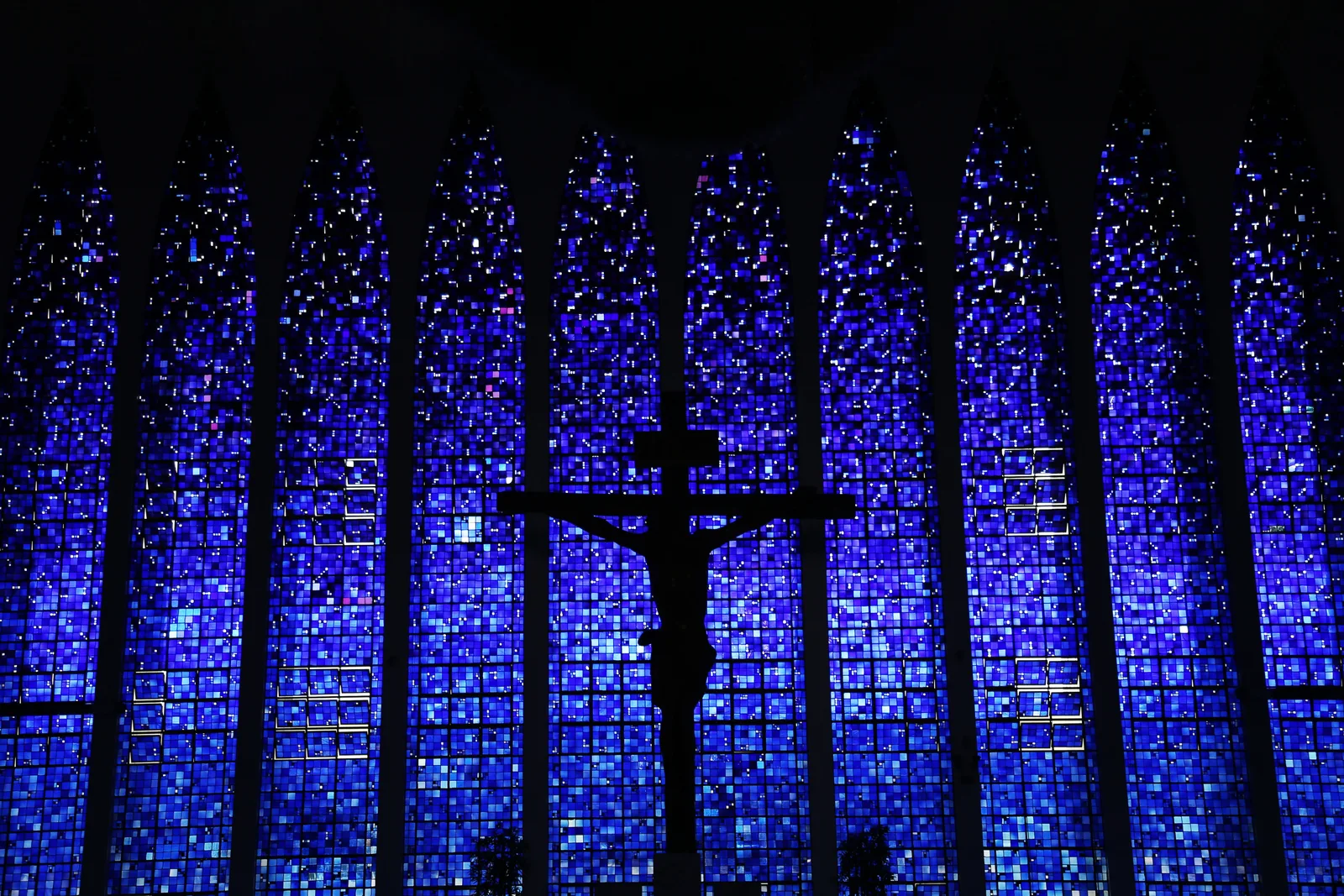 Inside the Santuário Dom Bosco: the sanctuary’s walls of deep blue glass rising between tall pointed arches, a crucifix silhouetted against the glass at the far end