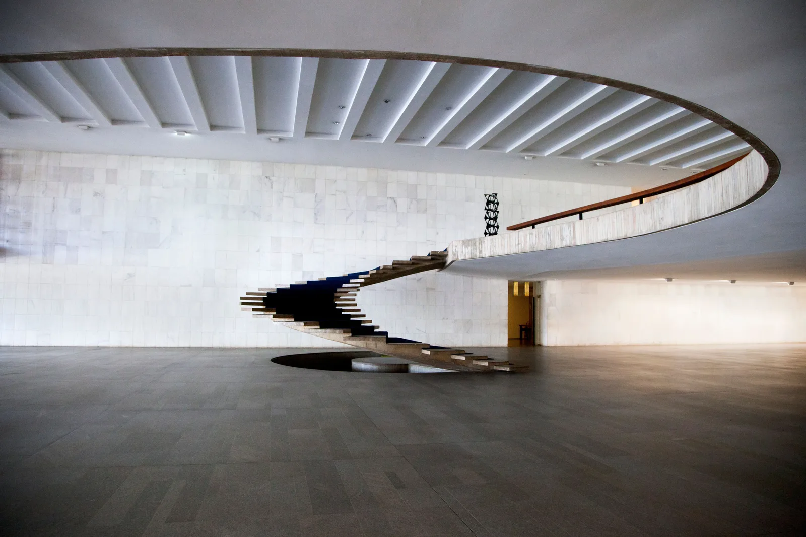 Oscar Niemeyer’s spiral staircase inside the Itamaraty Palace, a thin white concrete ribbon curving up without a handrail toward the slatted ceiling of a vast pale hall