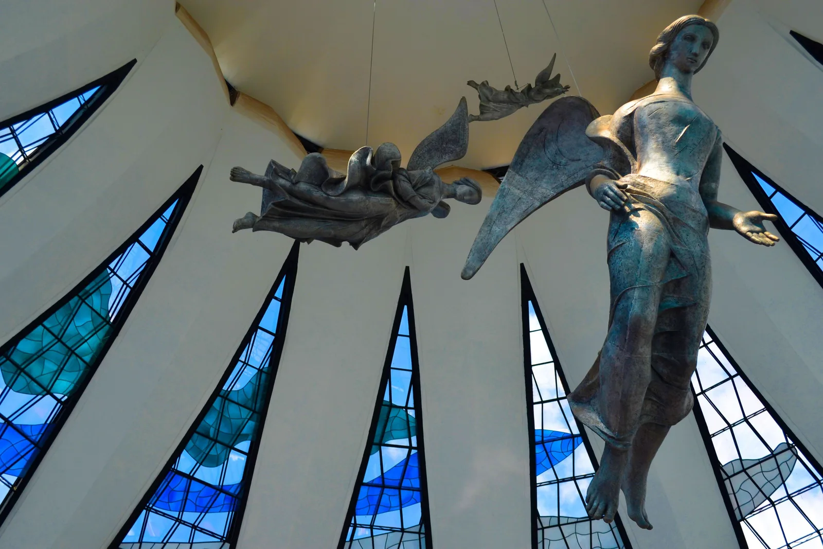 Alfredo Ceschiatti’s angels hanging on cables inside the Cathedral of Brasília, the white concrete ribs and Marianne Peretti’s blue and green stained glass behind them