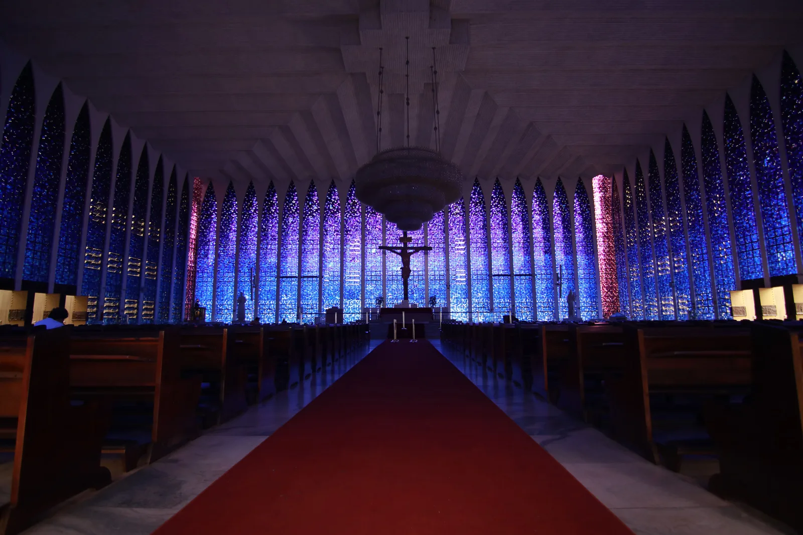 The nave of the Santuário Dom Bosco lit almost entirely blue by the sanctuary’s tall walls of blue glass, a red carpet running down the aisle between the pews