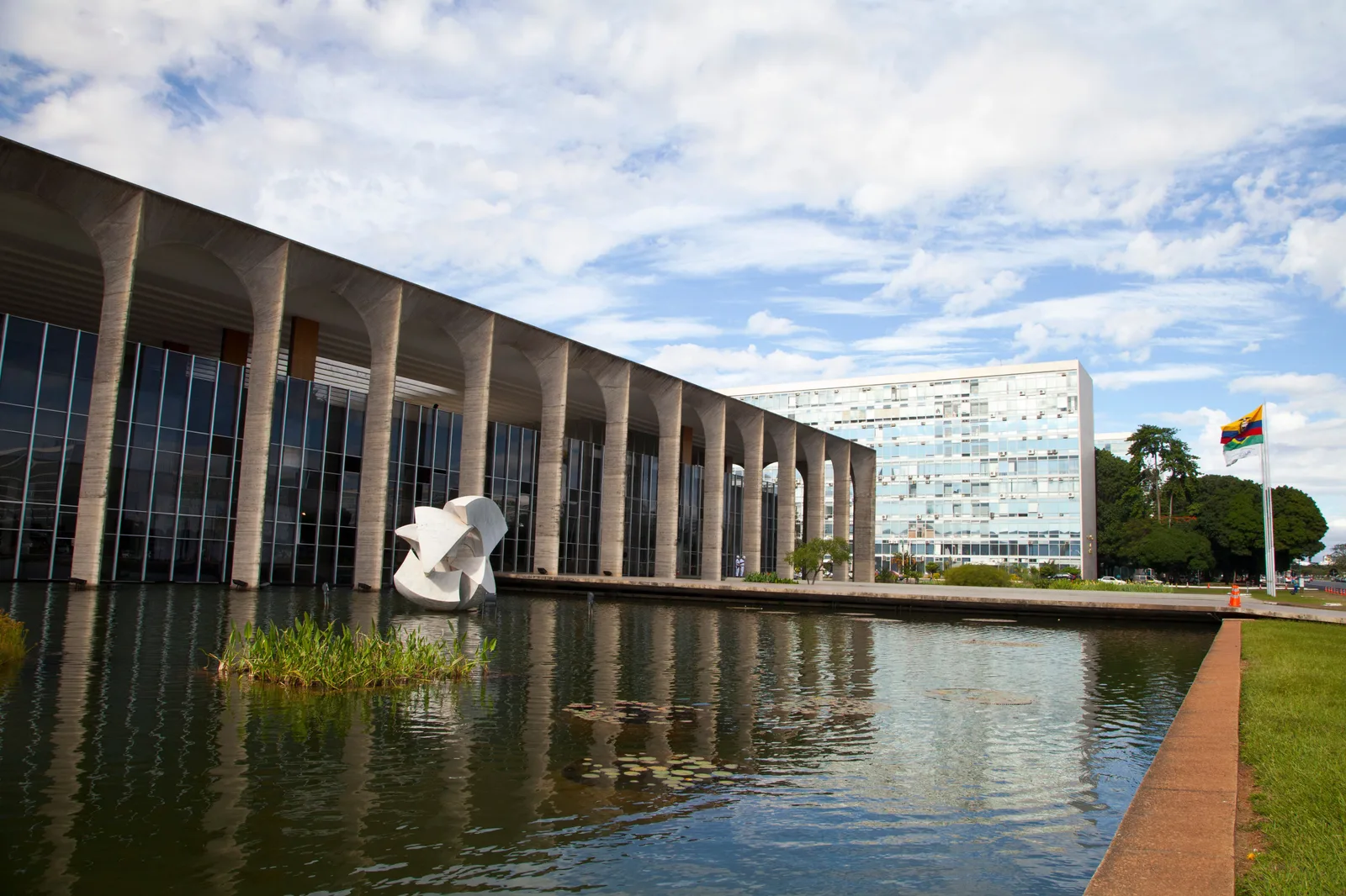 Bruno Giorgi’s white marble sculpture Meteoro standing in the reflecting pool of the Itamaraty Palace, the building’s tall concrete arches beside it