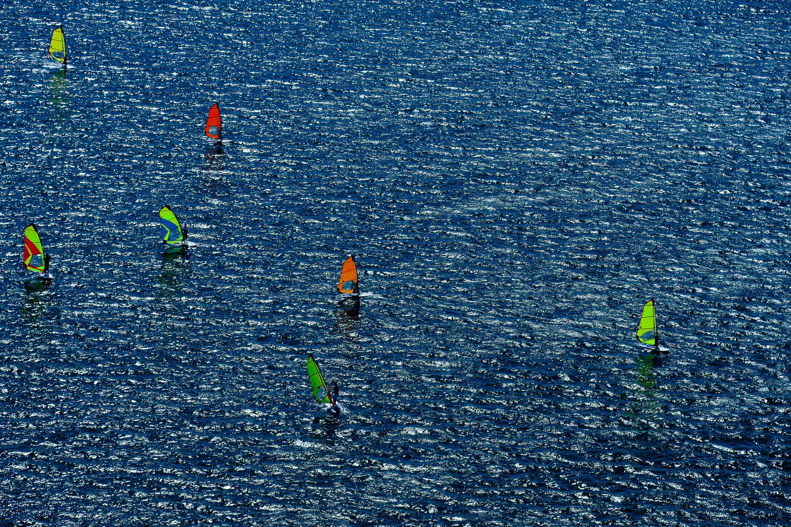 Windsurfers with bright sails crossing deep blue water on the lake in Brasília, seen from directly above