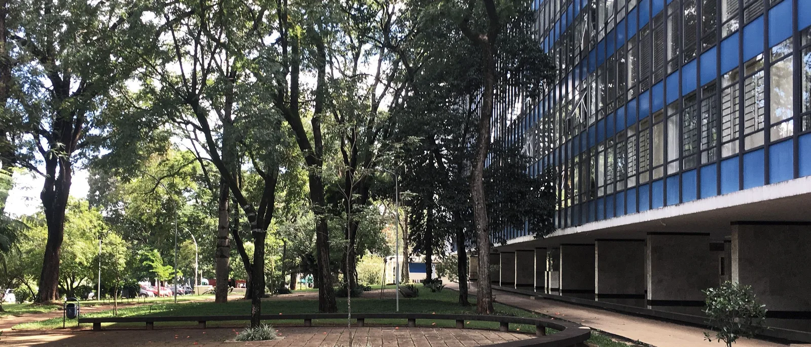 A superquadra in Asa Sul: an apartment block with blue-glazed windows raised over open ground behind a lawn, a curved bench and tall trees