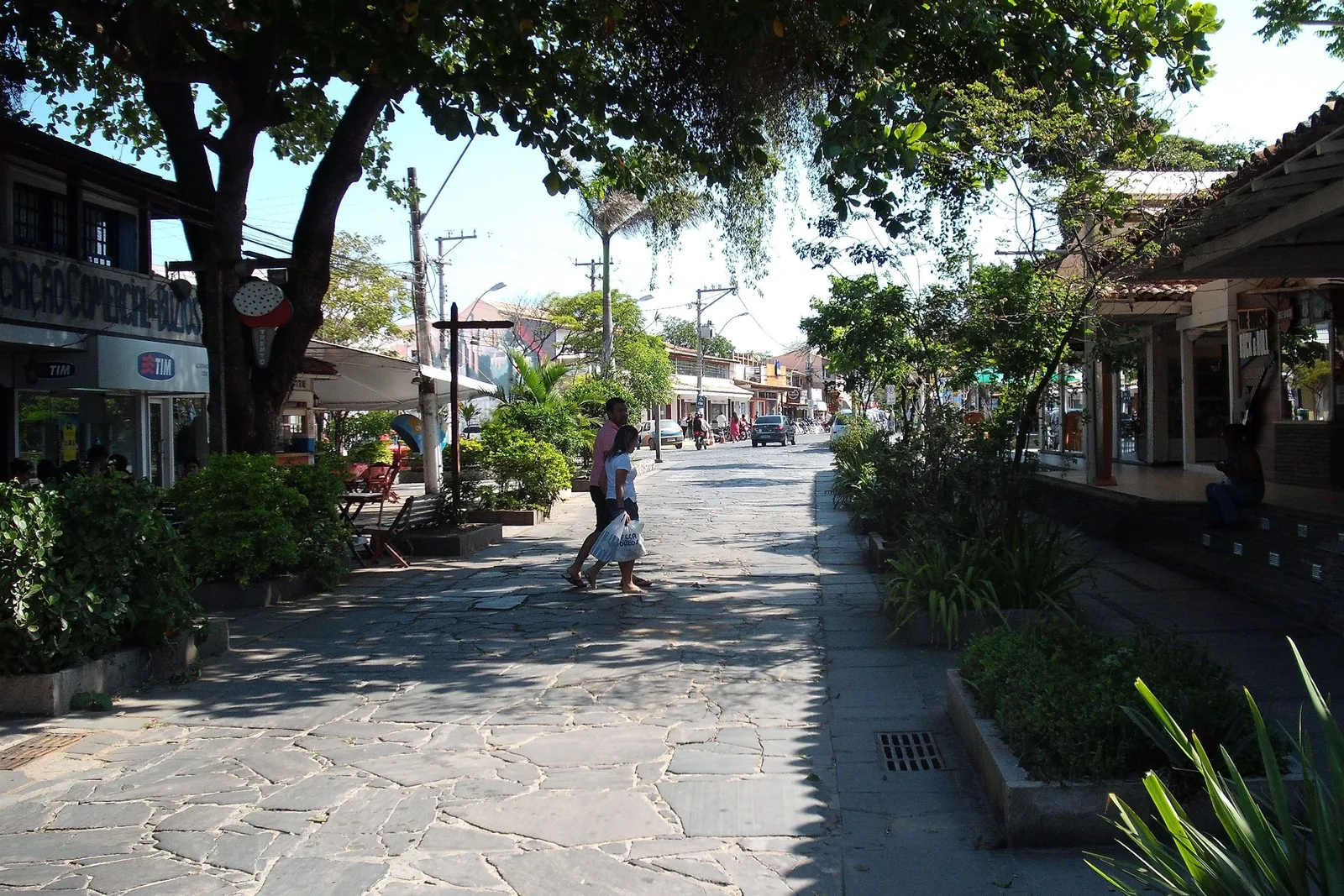 Rua das Pedras in Búzios: a street paved in irregular flat stones running between low shopfronts, with trees along one side and a few people walking down the middle