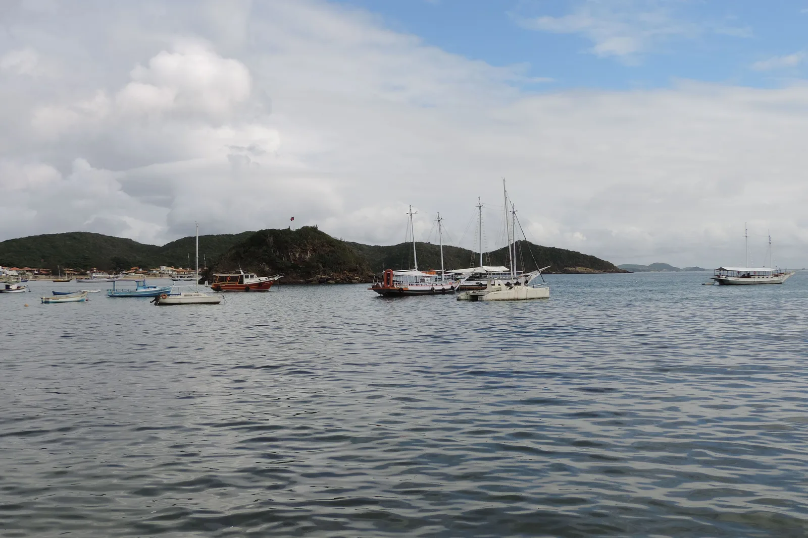 Two-masted wooden schooners and small launches at anchor in flat water in the bay at Búzios, with a low green headland behind