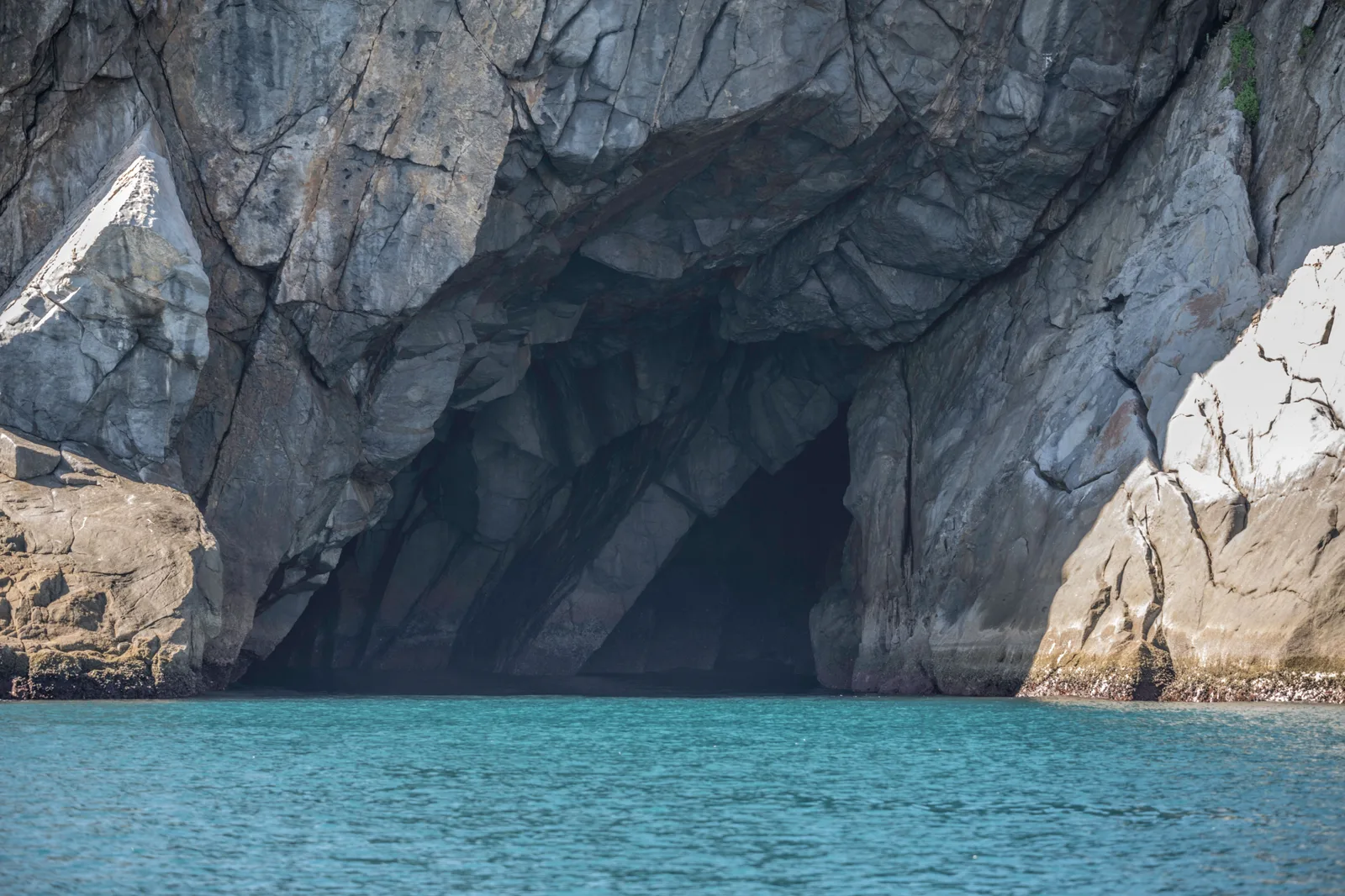 The dark mouth of a sea cave in gray angular rock at Arraial do Cabo, with bright turquoise water washing into it