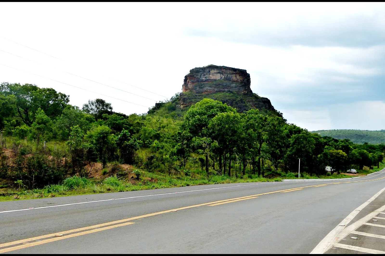 A paved highway curving toward a flat-topped rock hill with forest on both sides