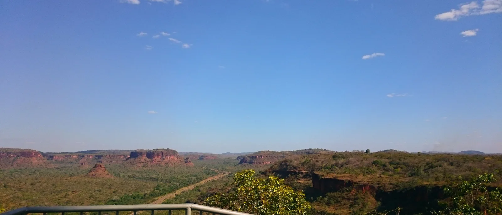 A viewing platform railing in the foreground and a wide valley of cerrado below, with red escarpments and mesas along the horizon
