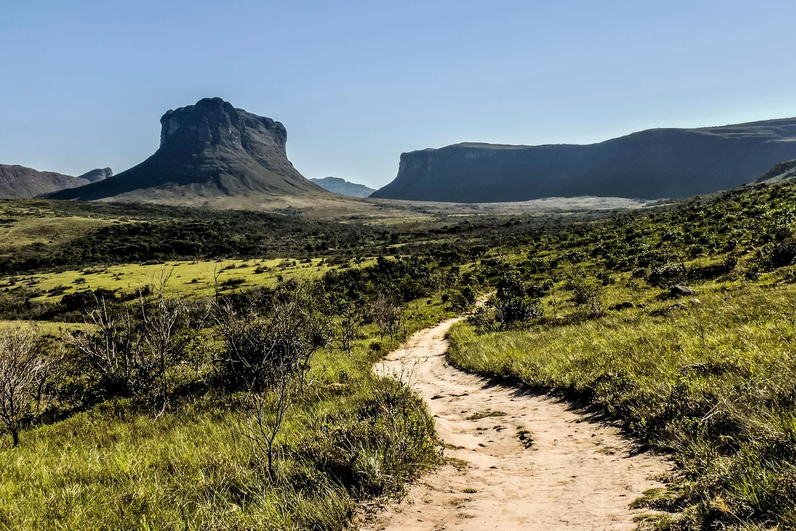 A sandy footpath curving through low green upland vegetation toward a blunt peak and a long flat-topped ridge