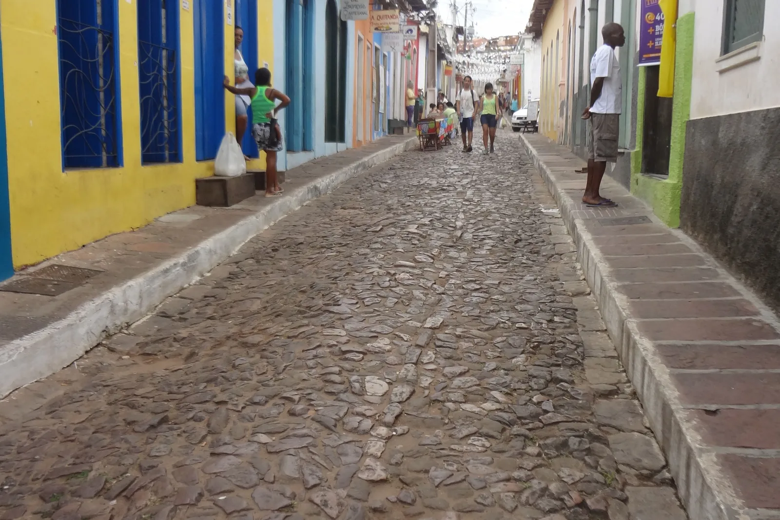 People walking up a cobbled street in Lençóis, the town in Bahia, between houses painted yellow, blue and green