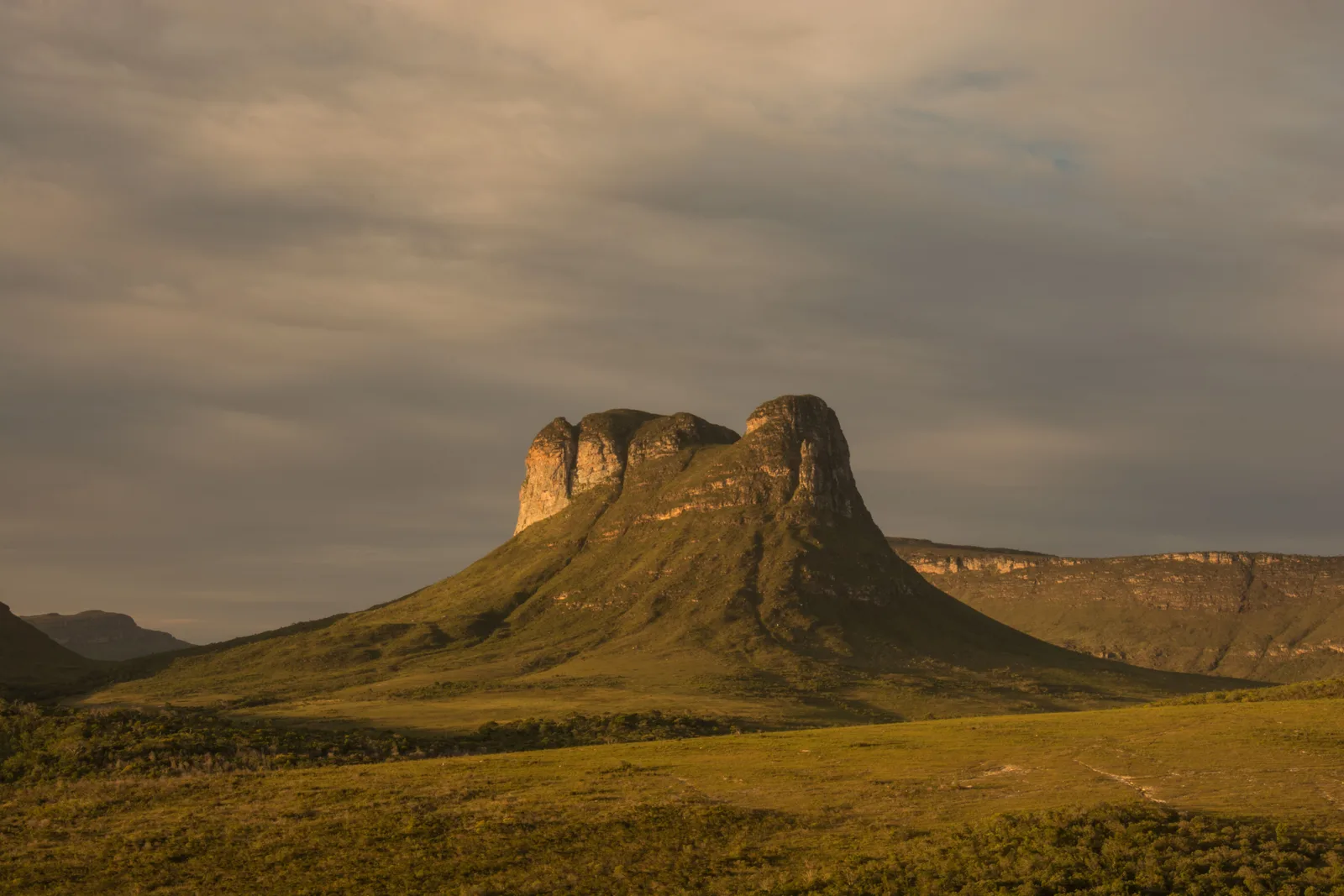 The flat-topped cone of the Morrão standing above dry grassland, its face lit gold under a heavy sky
