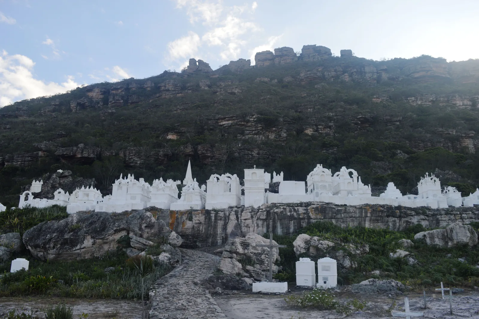 Rows of white pinnacled tombs spread along a rocky slope at the Santa Isabel cemetery in Mucugê, a bare stone ridge behind them
