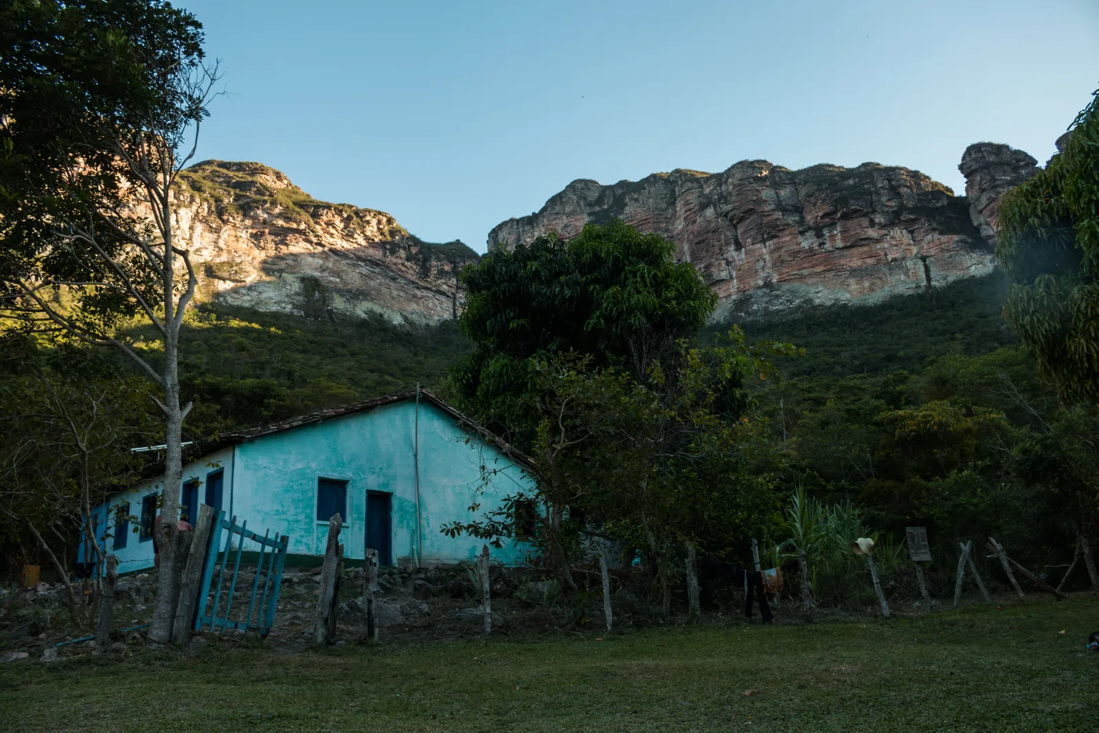 A small turquoise-painted house standing on the floor of the Vale do Pati with a wooded escarpment rising behind it