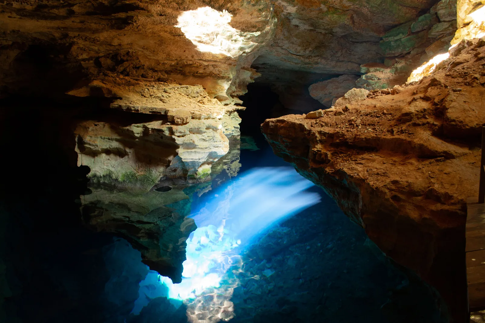 A shaft of daylight coming through the roof of a flooded cave and turning the water below it a vivid blue