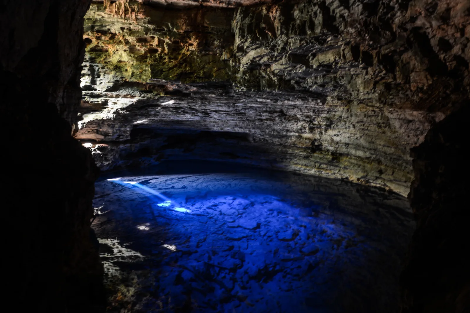 The deep blue lit water of Poço Encantado filling the floor of a dark cave chamber
