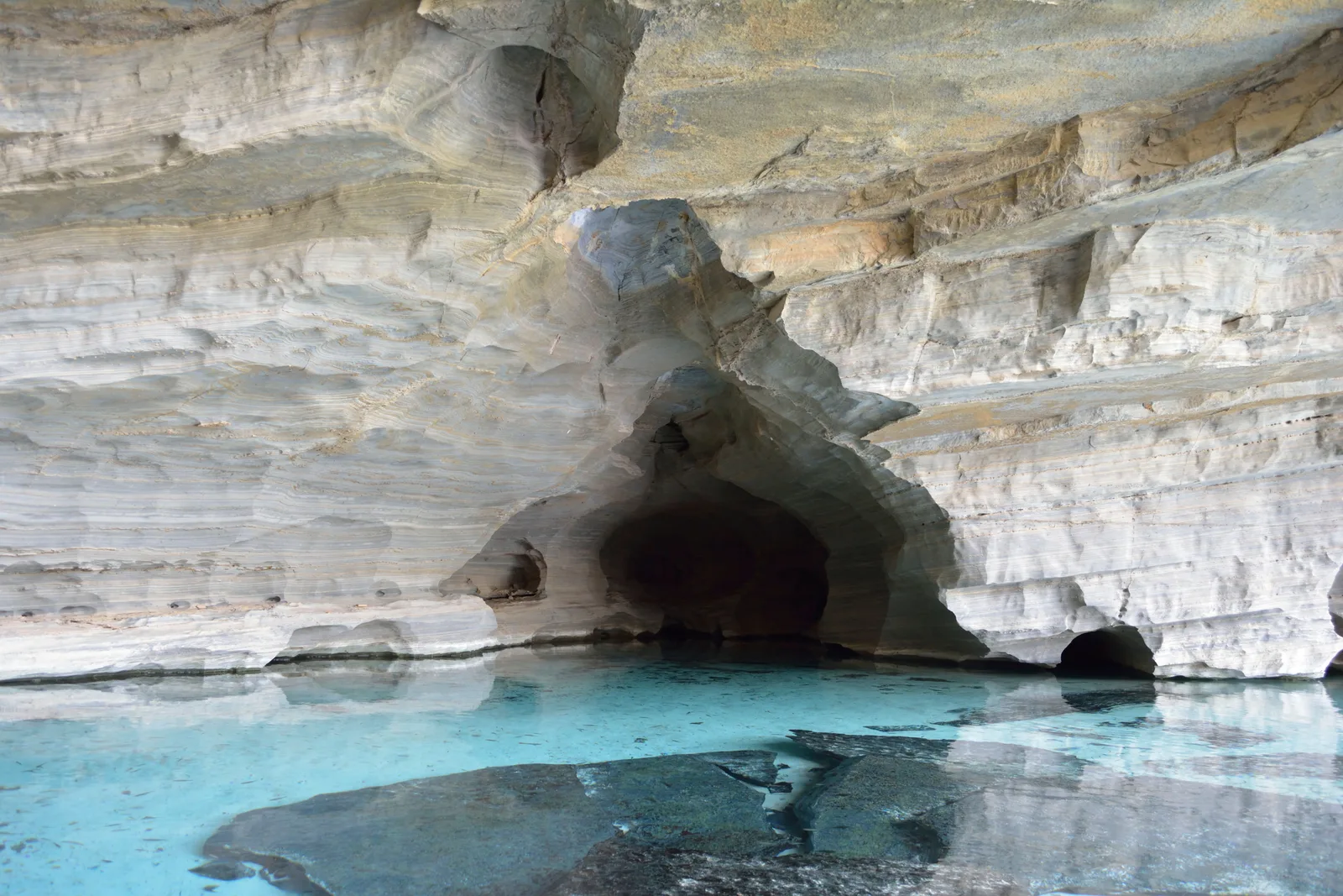 Clear turquoise water in the shallow pool at the mouth of the Pratinha cave, under a pale overhanging rock roof