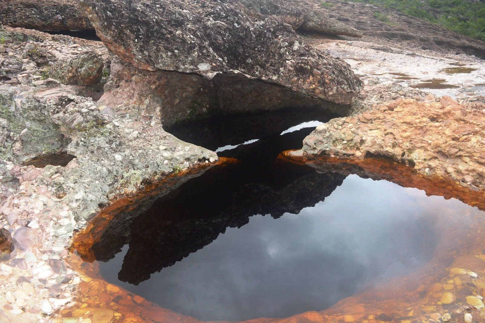 A round pool of dark tea-colored water scoured into orange-stained bedrock at the Serrano, beside Lençóis in Bahia