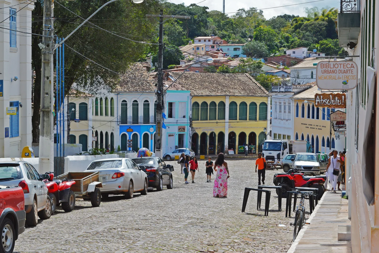 The main street of Lençóis, the town in Bahia, running downhill past an arcaded market building, cars parked along it and people crossing the cobbles