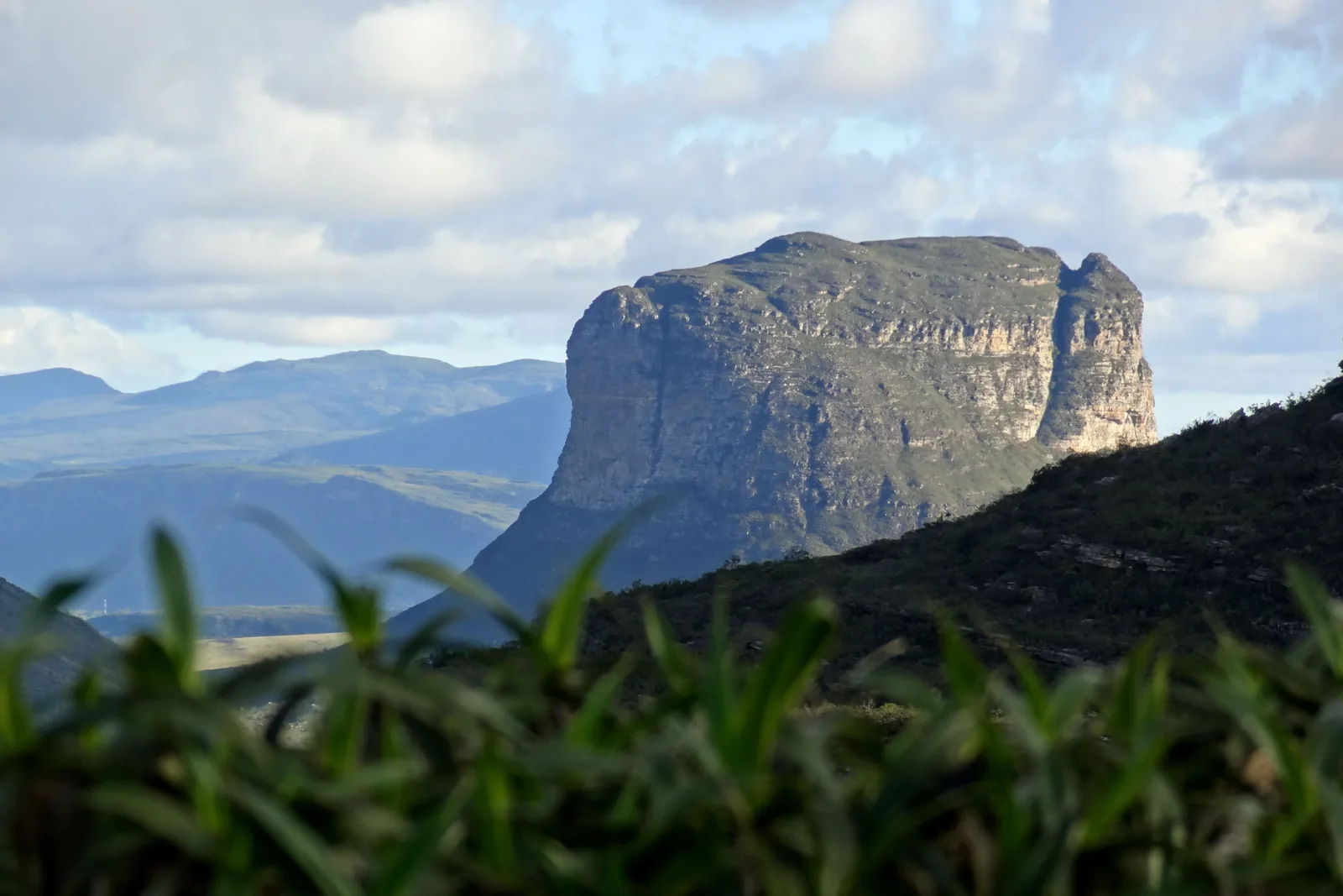 The Morrão seen across a green valley from Morro do Pai Inácio, its cliff face catching the afternoon light