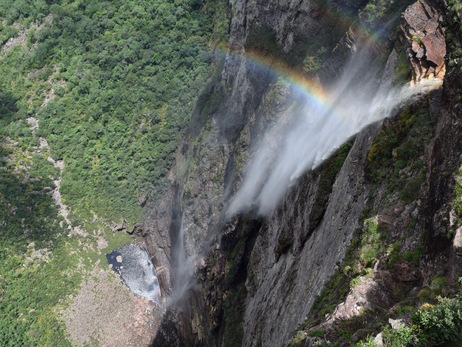 Looking down Cachoeira da Fumaça from the clifftop, the falling water breaking into spray with a rainbow in it and a small pool far below